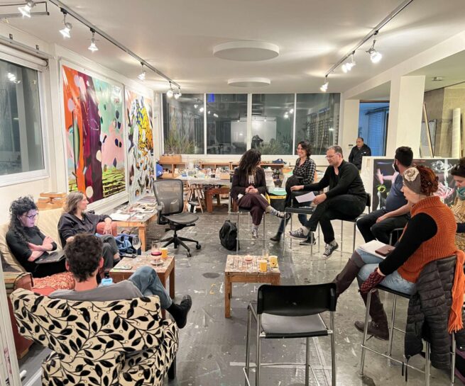 People sitting on an art studio. There are canvases with paintings